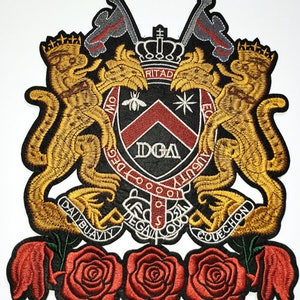 May include: Embroidered patch featuring a black shield with a red and white chevron, the letters "DGA" in white, and the text "DEUS" and "AUGUSTI" in white. The shield is flanked by two gold lions with crowns and a gold crown above the shield. Three red roses with green stems are at the bottom of the patch.