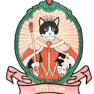 May include: An embroidered iron-on patch featuring a black and white cat wearing a crown and a red robe, holding a scepter. The cat is in a green oval frame with a pink background and the words "yth mus" on a pink banner.