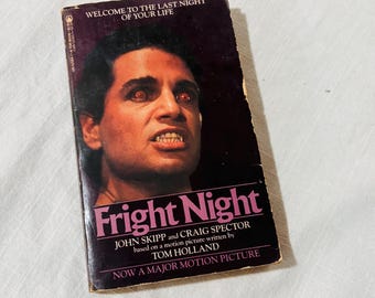 Puede incluir: Un libro de bolsillo titulado Fright Night de John Skipp y Craig Spector. La portada presenta un fondo morado oscuro con el retrato de una persona con ojos rojos brillantes y dientes afilados. El texto dice: Welcome to the last night of your life.