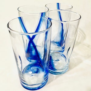 May include: Set of four clear glass drinking glasses with blue painted designs. The glasses are tall and cylindrical.