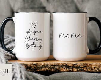 Może przedstawiać: Dwa białe ceramiczne kubki z czarnymi uchwytami i obwódkami. Jeden kubek ma napis "mama" w kursywie. Drugi kubek ma imiona "Andrew, Charley, Brittany" ze znakiem serca. Kubki stoją na drewnianej powierzchni.