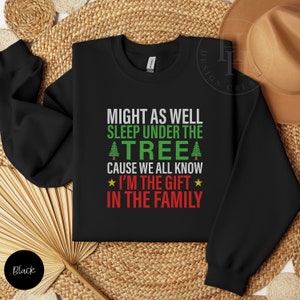 May include: Black sweatshirt with a Christmas-themed saying: "Might as well sleep under the tree cause we all know I'm the gift in the family".