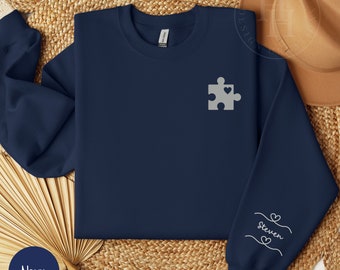 May include: Navy blue sweatshirt with a gray puzzle piece with a heart on it. The left sleeve has the word "Steven" written in gray with hearts on either side.