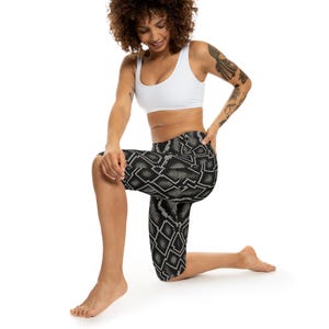 Könnte beinhalten: Schwarze und graue Capri-Leggings mit Muster. Die Leggings haben ein geometrisches Design in Schwarz-, Grau- und Weißtönen. Das Model trägt einen weißen Sport-BH. Die Leggings sind knielang und figurbetont.