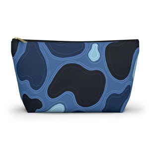 May include: A zippered cosmetic bag with a blue abstract pattern. The pattern features dark blue, navy, and light blue organic shapes. The bag has a black zipper and a black interior.