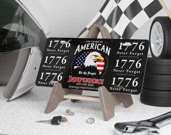 May include: A black license plate with the text "1776 Never Forget" and "American Independence July 4th 2026" displayed on a wooden stand. The plate features an American flag and an eagle. A checkered flag and tires are in the background.