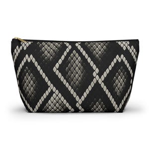May include: A black cosmetic bag with a snakeskin pattern in shades of gray and white. The bag has a gold zipper closure and a rectangular shape. The pattern is a repeating diamond design.