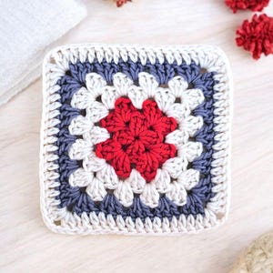 May include: A crocheted square with a red and white center and a blue and white border.