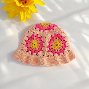 Könnte beinhalten: Ein gehäkelter Bucket-Hut mit einem floralen Muster in Rosa, Gelb und Orange.