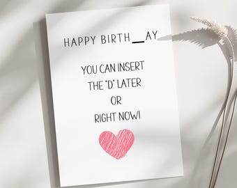 May include: White greeting card with the text "HAPPY BIRTH__AY" and "YOU CAN INSERT THE 'D' LATER OR RIGHT NOW!". A pink heart is drawn at the bottom. The card is on a white surface.