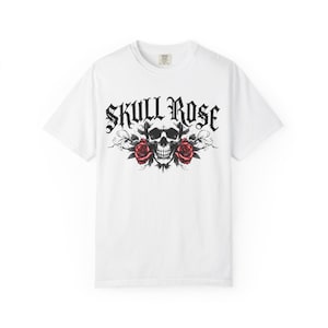 Puede incluir: Camiseta blanca con un diseño gráfico que presenta una calavera, dos rosas rojas y las palabras "SKULL ROSE" en una fuente gótica. El diseño está centrado en la parte delantera de la camiseta.
