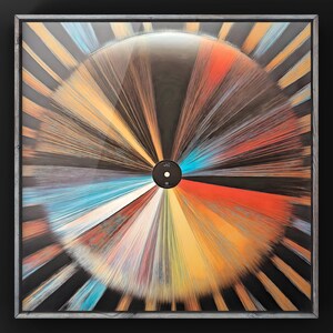May include: A framed artwork featuring a colorful, radial design resembling a record. The design is made up of thin, colorful lines radiating from the center, creating a dynamic and abstract pattern. The center of the design features a small, black circle with the word "LMI" printed on it.