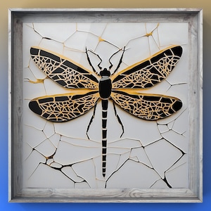 Könnte beinhalten: Eine gerahmte schwarze und goldene Libelle mit filigranen Flügeldetails vor einem weißen, rissigen Hintergrund.