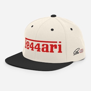 Könnte beinhalten: Eine cremefarbene Baseballkappe mit schwarzem Schirm und einem schwarzen Knopf an der Oberseite. Auf der Vorderseite befindet sich der rote Schriftzug "Fe44ari" mit einer horizontalen Linie darüber. Die Seite zeigt eine schwarze Stickerei und die rote Zahl 44.