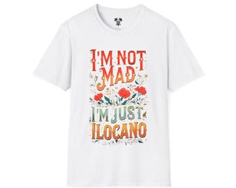 May include: White t-shirt with the text "I'M NOT MAD I'M JUST ILOCANO" in a colorful, floral design. The text is in red, orange, and green, with red flowers and green leaves. A casual, everyday wear tee.