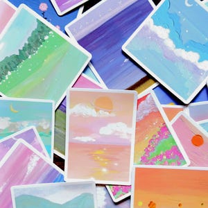 Puede incluir: Una colección de coloridas impresiones artísticas con pinturas de paisajes. Las impresiones muestran varias escenas, incluyendo puestas de sol, montañas y cuerpos celestes. La obra de arte está realizada en un estilo pictórico con colores suaves y una estética de ensueño.