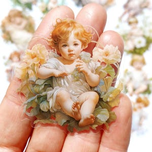 May include: A clear sticker featuring a vintage illustration of a baby angel with blonde hair, wearing a white dress and sitting amongst white flowers and green leaves.