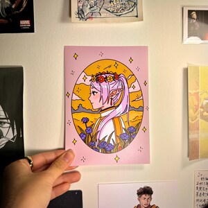 May include: A pink background with a circular illustration of a female character with lavender hair wearing a flower crown and a white and yellow outfit. The character is surrounded by a field of yellow and blue flowers. The background is a yellow sunset with clouds.