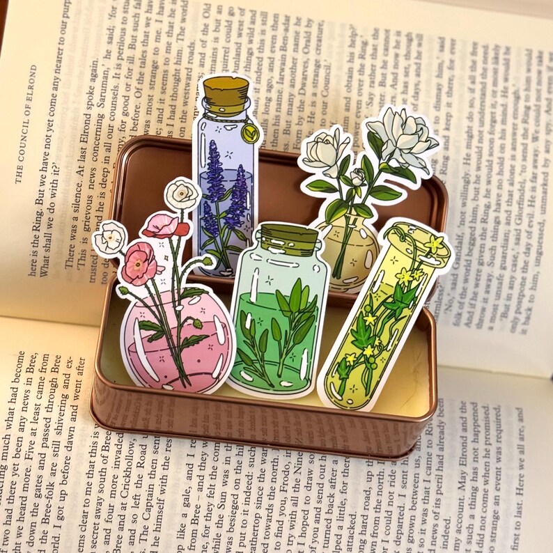 May include: A collection of decorative stickers featuring various floral arrangements in glass containers. The stickers showcase different flowers and greenery in vases and jars, with a vintage aesthetic. The stickers are arranged on a book.