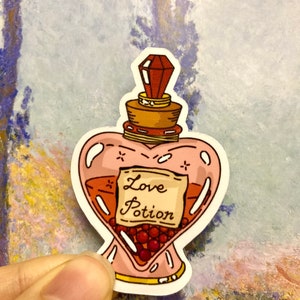 May include: A pink heart-shaped glass bottle with a red stopper and a label that reads "Love Potion". The bottle is filled with a red liquid and small red berries.