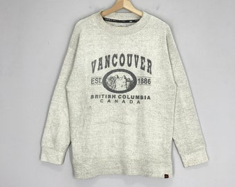 May include: A light gray sweatshirt with a black graphic print that says "Vancouver Est. 1886 British Columbia Canada". The graphic also includes a black and white image of a mountain range with a wolf.