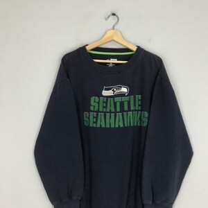 Puede incluir: Sudadera negra con un logotipo de los Seattle Seahawks en verde y blanco y las palabras "Seattle Seahawks" en verde.