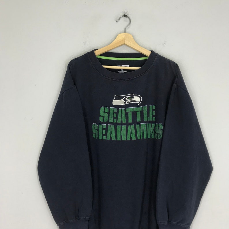 Puede incluir: Sudadera negra con un logotipo de los Seattle Seahawks en verde y blanco y las palabras "Seattle Seahawks" en verde.