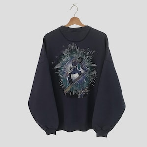 Op de afbeelding: Een donkerblauw sweatshirt met een grafische print van een persoon die snowboardt. De grafiek is in tinten blauw, groen en wit.