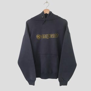 May include: A dark blue hooded sweatshirt with a gold and black logo that says "snapcase".