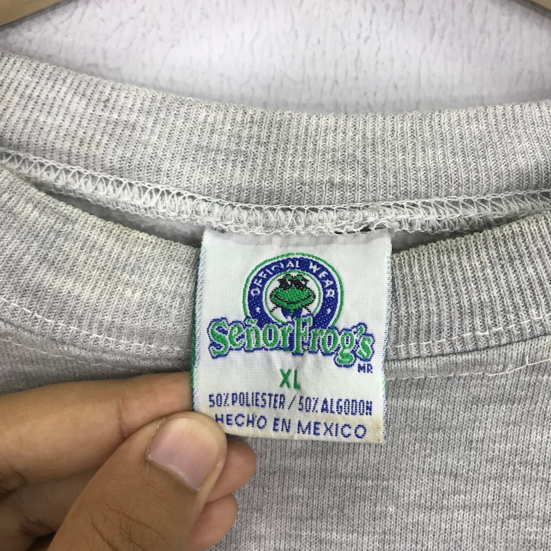 May include: Gray sweatshirt with a tag that says "Official Wear Se&ntilde;or Frog's" in a circle with a green frog inside. The tag also says "XL" and "50% Polyester / 50% Algodon Hecho en Mexico".