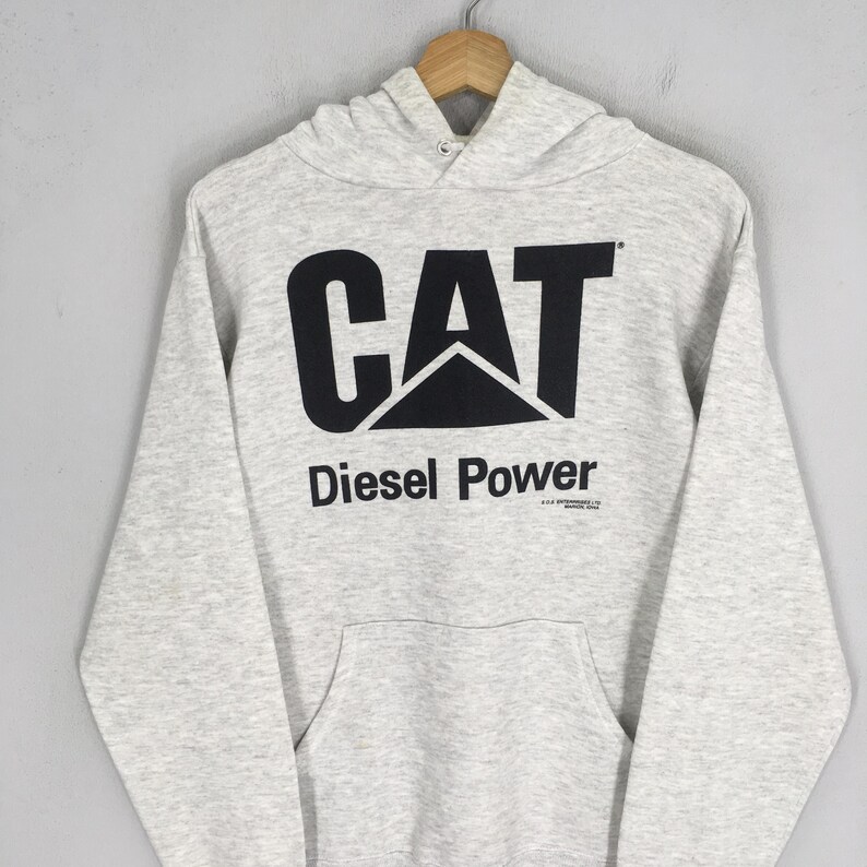 Puede incluir: Una sudadera con capucha de manga larga en color gris jaspeado claro que presenta un gran logotipo CAT negro impreso en el pecho con el texto Diesel Power debajo. La prenda incluye un bolsillo tipo canguro y capucha con cord&oacute;n.