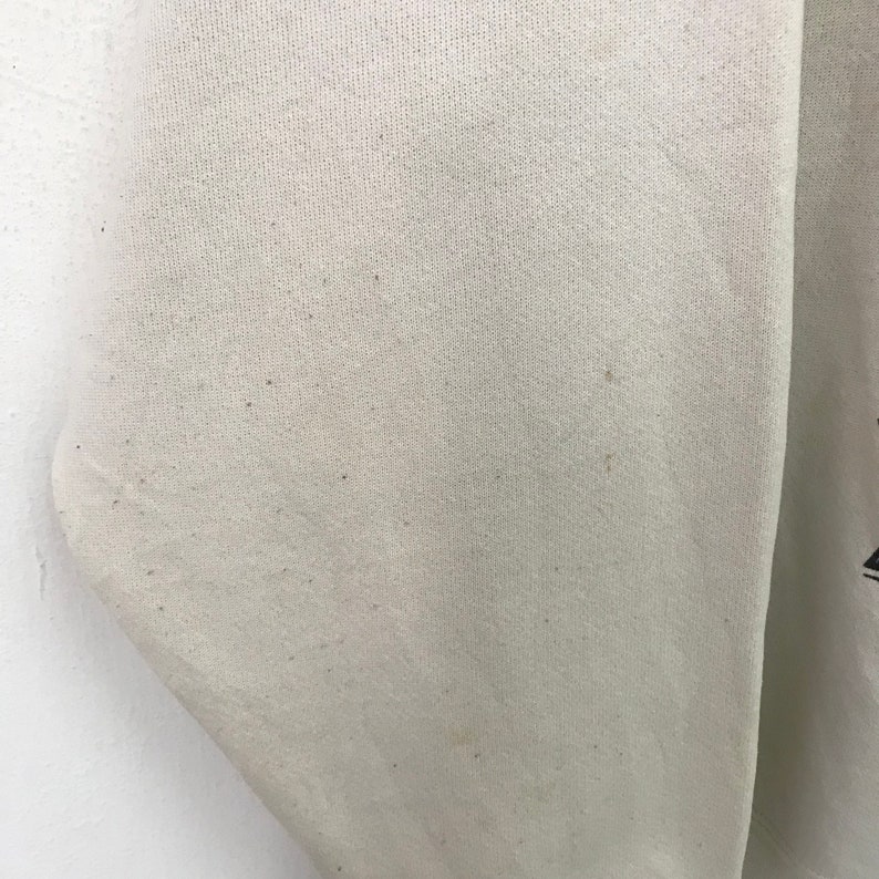 May include: Close-up of a white sweatshirt with a slightly textured surface. The fabric has a few small brown spots.