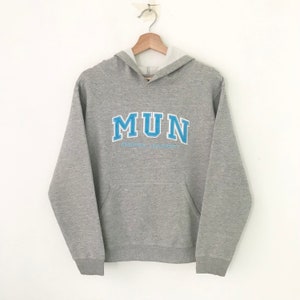 Könnte beinhalten: Grauer Kapuzenpullover mit einem blau-weißen Logo, auf dem "MUN" und "MEMORIAL UNIVERSITY" steht.