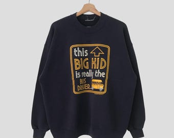 以下が含まれることがあります： 黄色いスクールバスのイラストと「this BIG KID is really the BUS DRIVER」と書かれた黄と白のグラフィックが特徴の、ネイビーブルーのスウェットシャツ。木製のハンガーにかかっています。