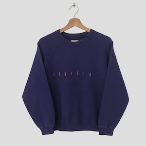 Puede incluir: Una sudadera de color morado oscuro con un logotipo "BENETTON" bordado en arcoíris en la parte delantera.