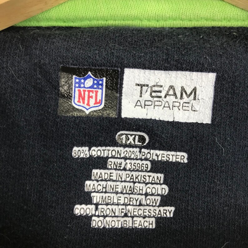 Puede incluir: Una camiseta polo negra NFL Team Apparel talla 1XL con cuello verde. La camiseta est&aacute; hecha de 80% algod&oacute;n y 20% poli&eacute;ster. Las instrucciones de cuidado son: Lavar a m&aacute;quina con agua fr&iacute;a, secar en secadora a baja temperatura, planchar a baja temperatura si es necesario, no usar lej&iacute;a.