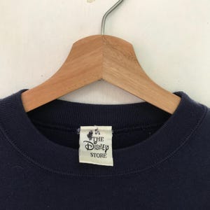 May include: A navy blue sweatshirt with a white tag that reads "The Disney Store".