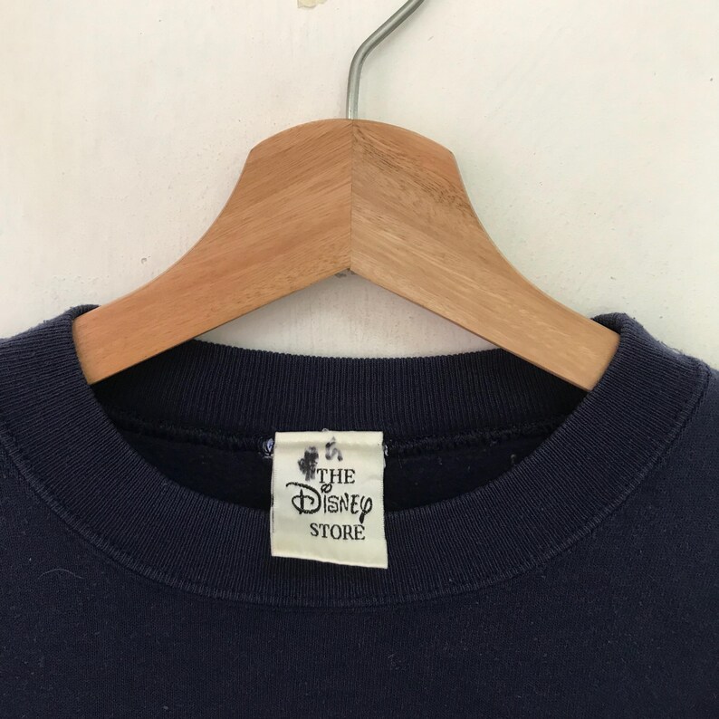May include: A navy blue sweatshirt with a white tag that reads "The Disney Store".