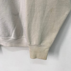 May include: A close-up of the cuff of a light beige sweatshirt. The fabric is soft and has a slightly textured appearance.
