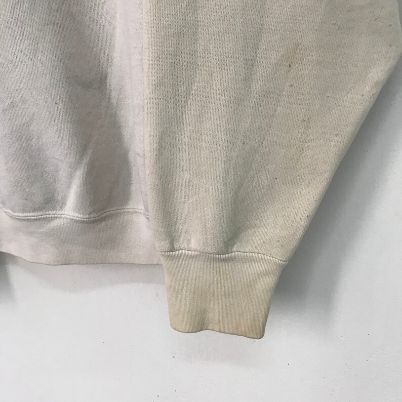 May include: A close-up of the cuff of a light beige sweatshirt. The fabric is soft and has a slightly textured appearance.