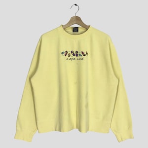 Könnte beinhalten: Gelber Pullover mit einem Aufdruck von Flip-Flops und dem Text "cape cod" auf der Vorderseite.