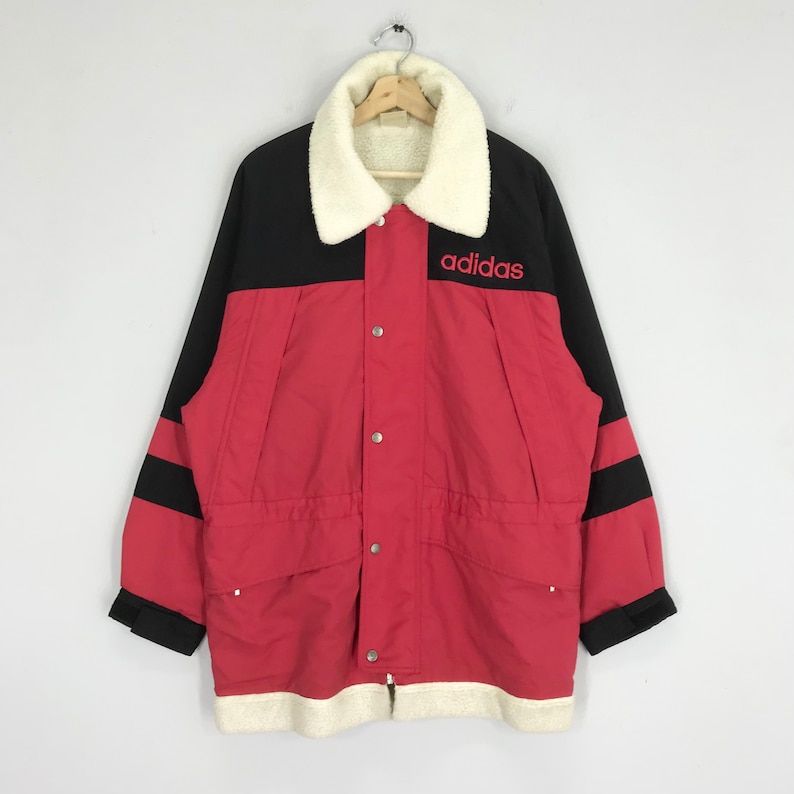 May include: A red and black Adidas jacket with a white fleece collar and black stripes on the sleeves. The jacket has a button closure and a drawstring waist. The Adidas logo is embroidered on the right chest in red.