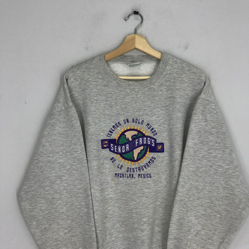 May include: Gray sweatshirt with a graphic of a globe with the text "Tenemos un solo mundo" and "Send Frog's" in a circle around it. The text "No lo destruyamos" and "Mazatlan, Mexico" are below the globe.