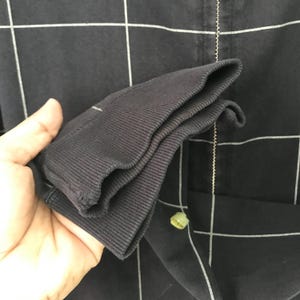 May include: A black and white checkered zip-up jacket with a folded cuff. The jacket is made of a soft, comfortable fabric.