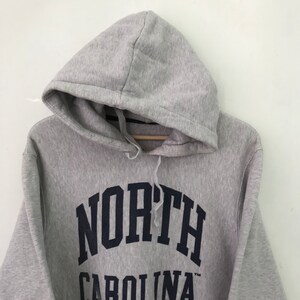 May include: Gray hooded sweatshirt with a navy blue arch design that reads "NORTH CAROLINA" in a collegiate font.