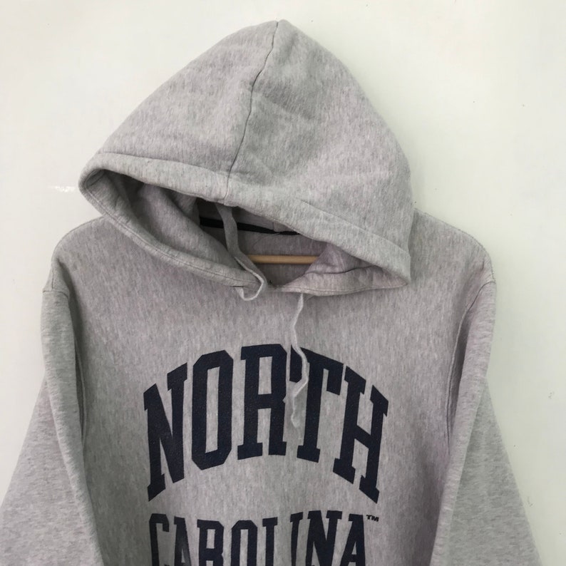 May include: Gray hooded sweatshirt with a navy blue arch design that reads "NORTH CAROLINA" in a collegiate font.