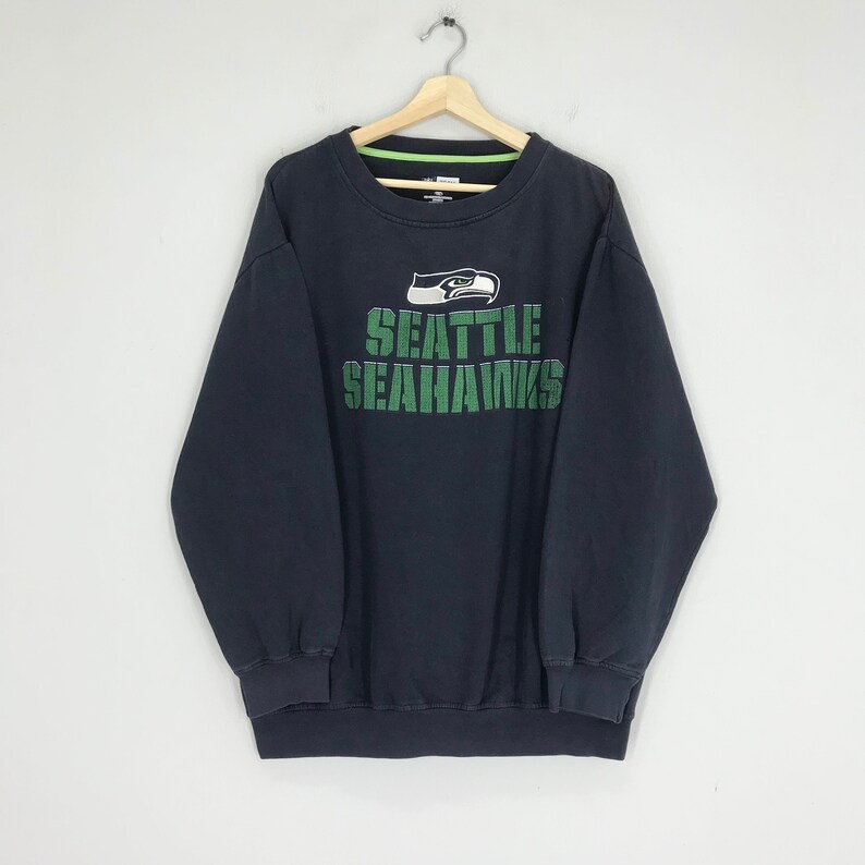 Puede incluir: Sudadera negra con un logotipo y texto de los Seattle Seahawks en verde.