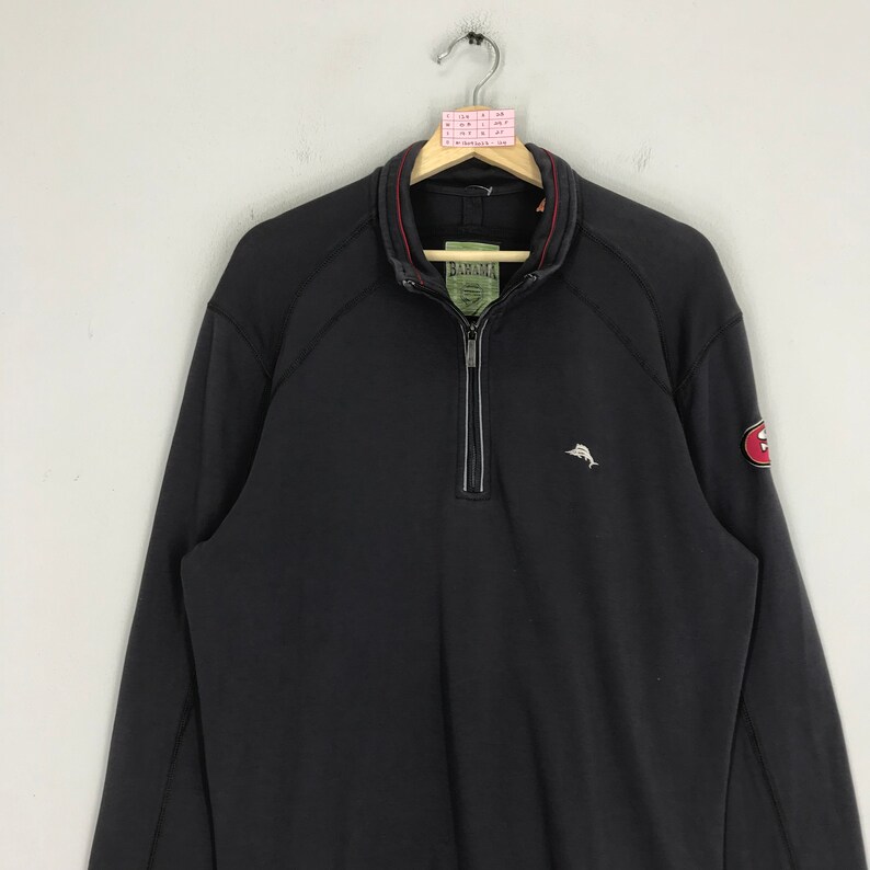 Peut inclure: Sweat-shirt noir &agrave; fermeture &eacute;clair quart avec un petit logo de dauphin brod&eacute; sur la poitrine gauche et un patch rouge avec un logo blanc sur la manche droite. Le sweat-shirt a une fermeture &eacute;clair rouge et une bordure rouge autour du col.