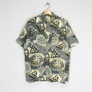 May include: A short-sleeved button-down shirt with a grey background and a colourful geometric pattern. The pattern features brown, white, and yellow colours.