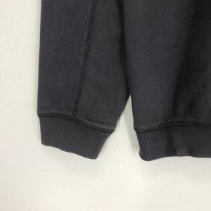 Peut inclure: Un sweat-shirt gris fonc&eacute; &agrave; manches longues et poignets c&ocirc;tel&eacute;s. Le sweat-shirt a un design uni sans graphismes ni texte visibles.
